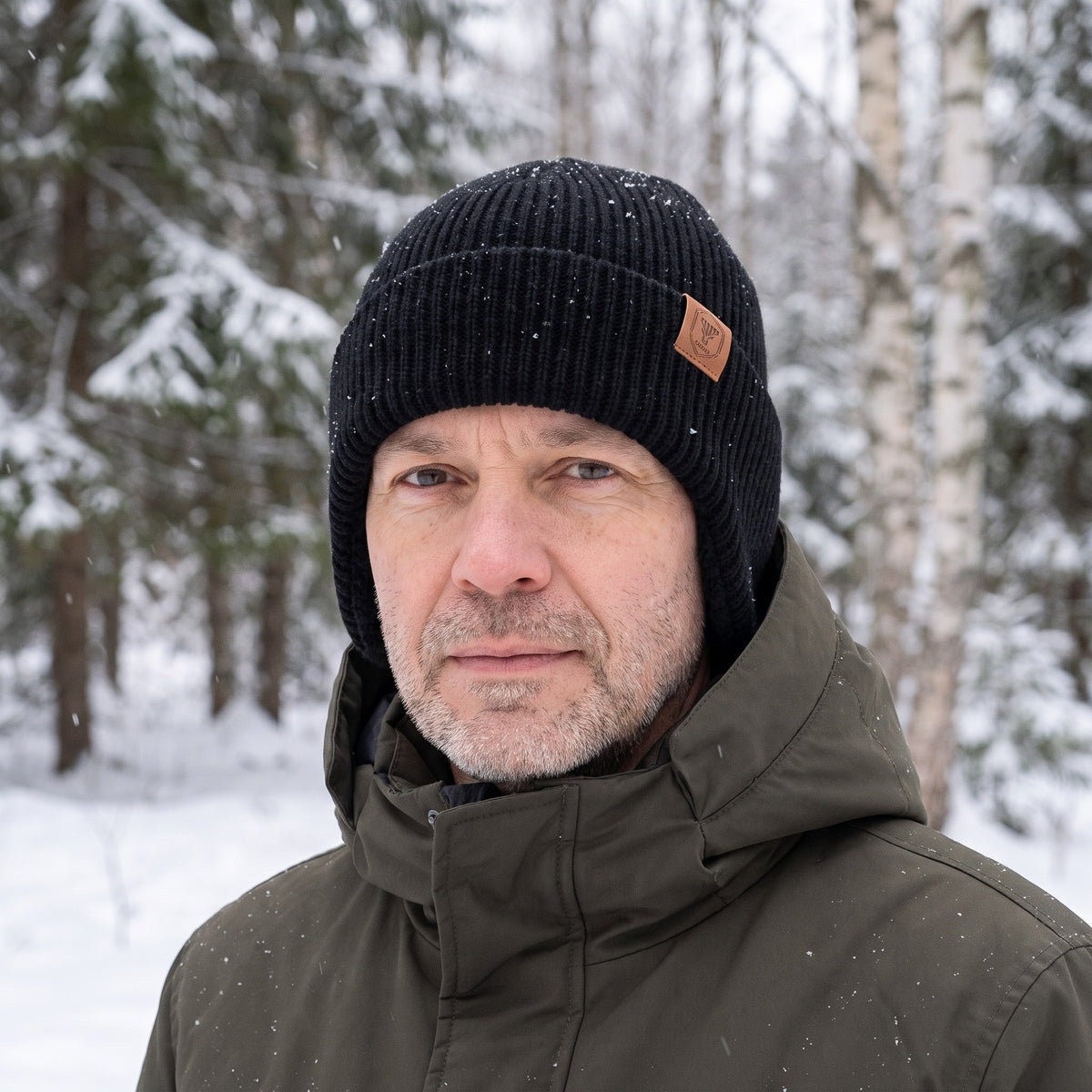Hue med øreklapper i sort båret i en snedækket skov